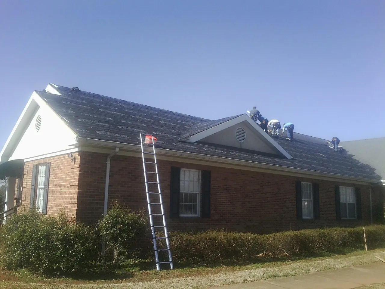 Crew tearing shingles off a brick ranch roof with a ladder set — Emergency Roof Repair work by our crew in Carrsville