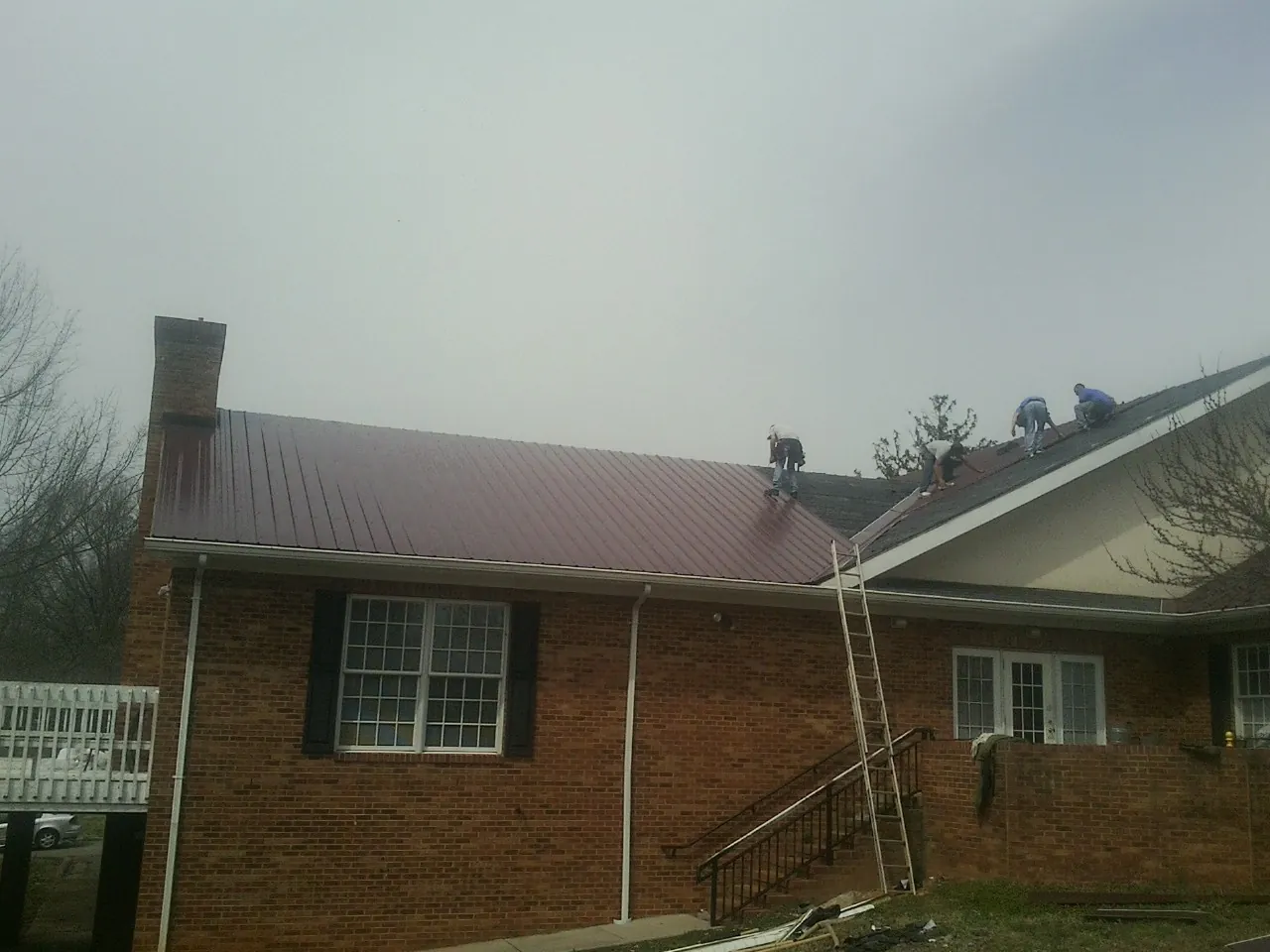 Crew setting red metal roofing panels on a brick home in Carrsville