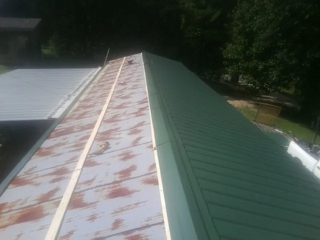 Old rusted panels beside newly installed green metal roofing — Wind Damage Roof Repair by Roofing Brothers in Carrsville