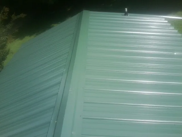 New green metal panels meeting at the ridge of a roof — Flat Roof Repair work by our crew in Carrsville