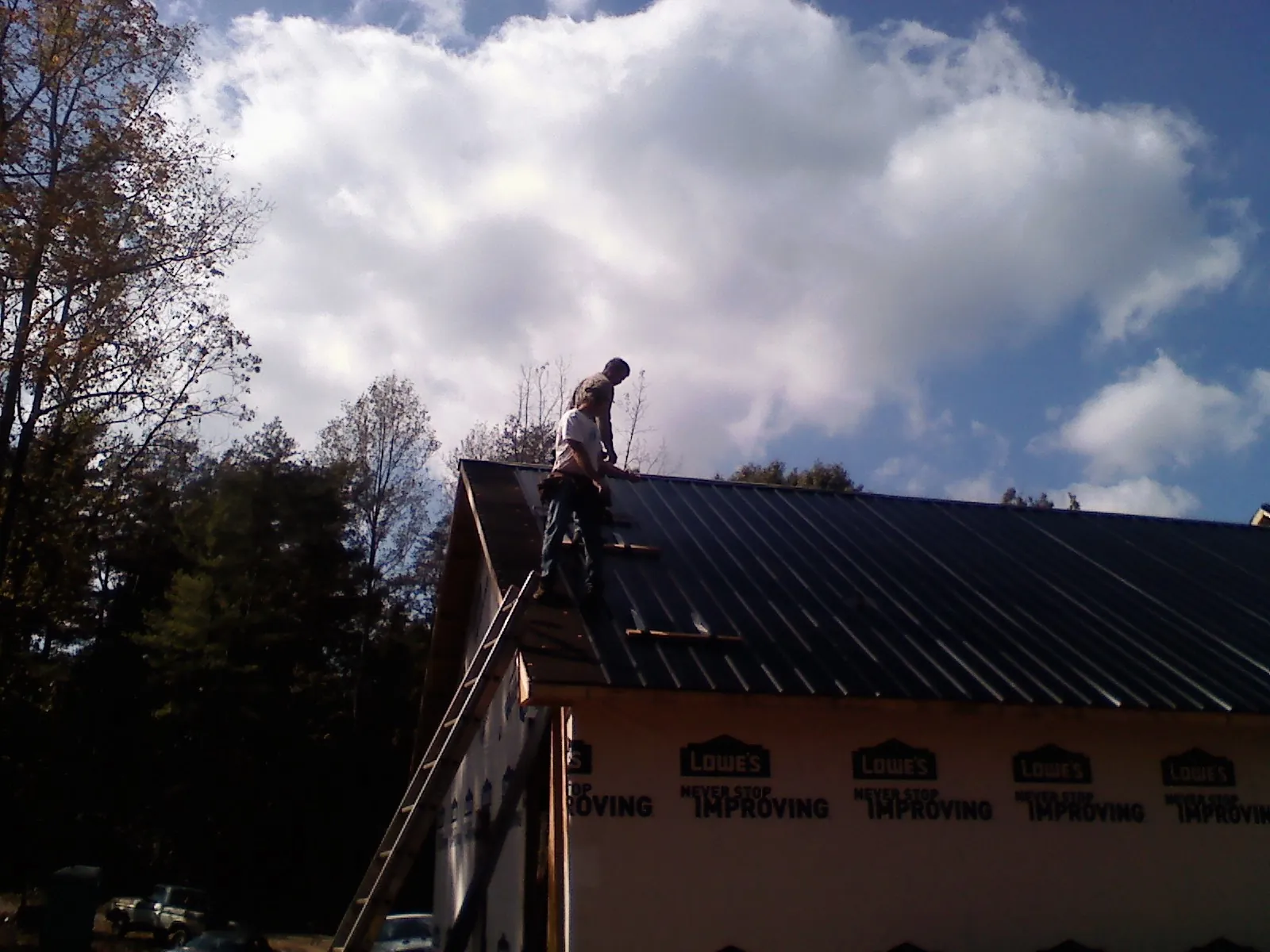 Roofer fastening dark metal panels high against a cloudy sky, from a Roof Inspection job in Carrsville
