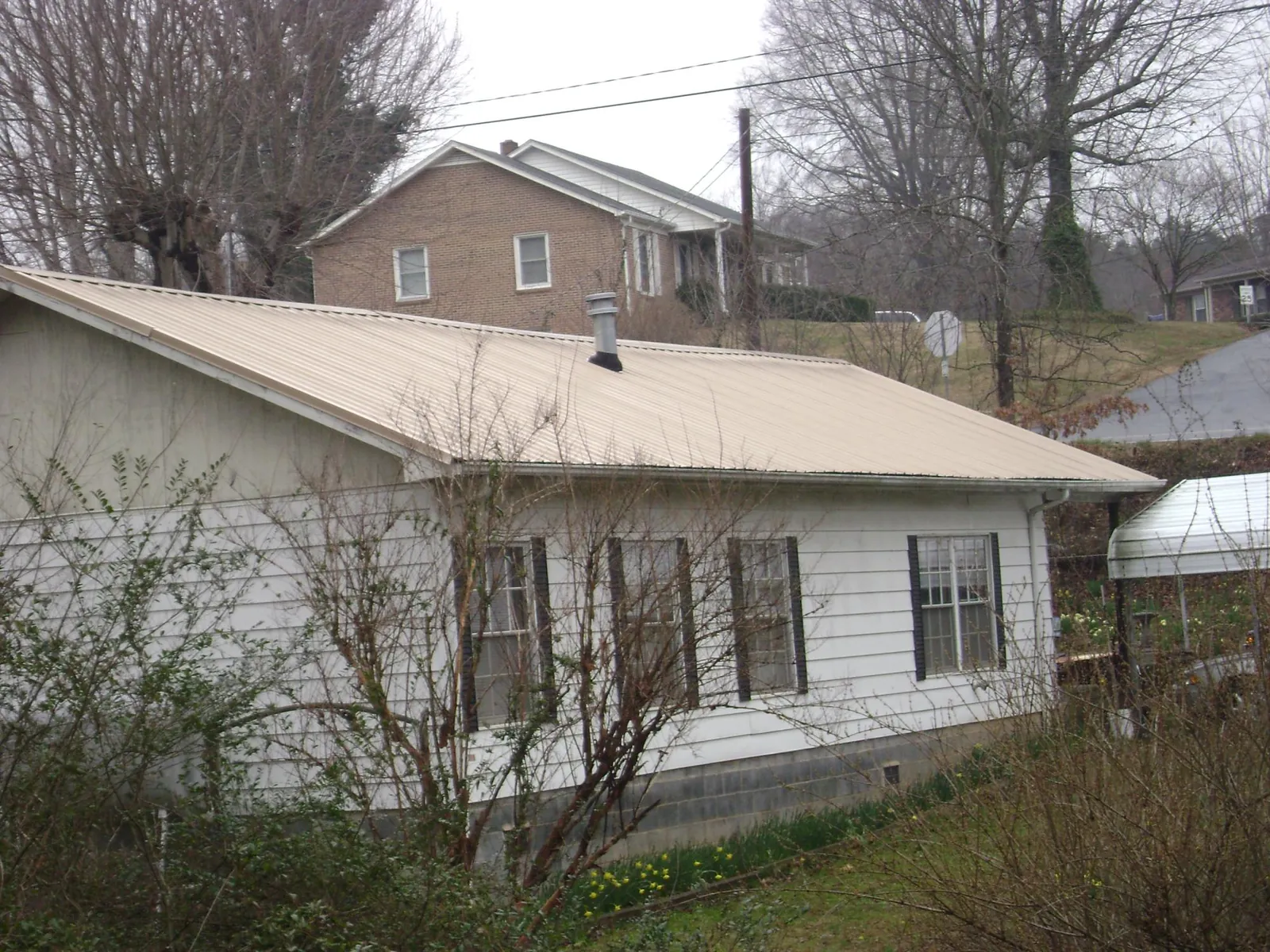 Tan metal roof on a white sided house set into a hillside — Commercial Roofing by Roofing Brothers in Carrsville