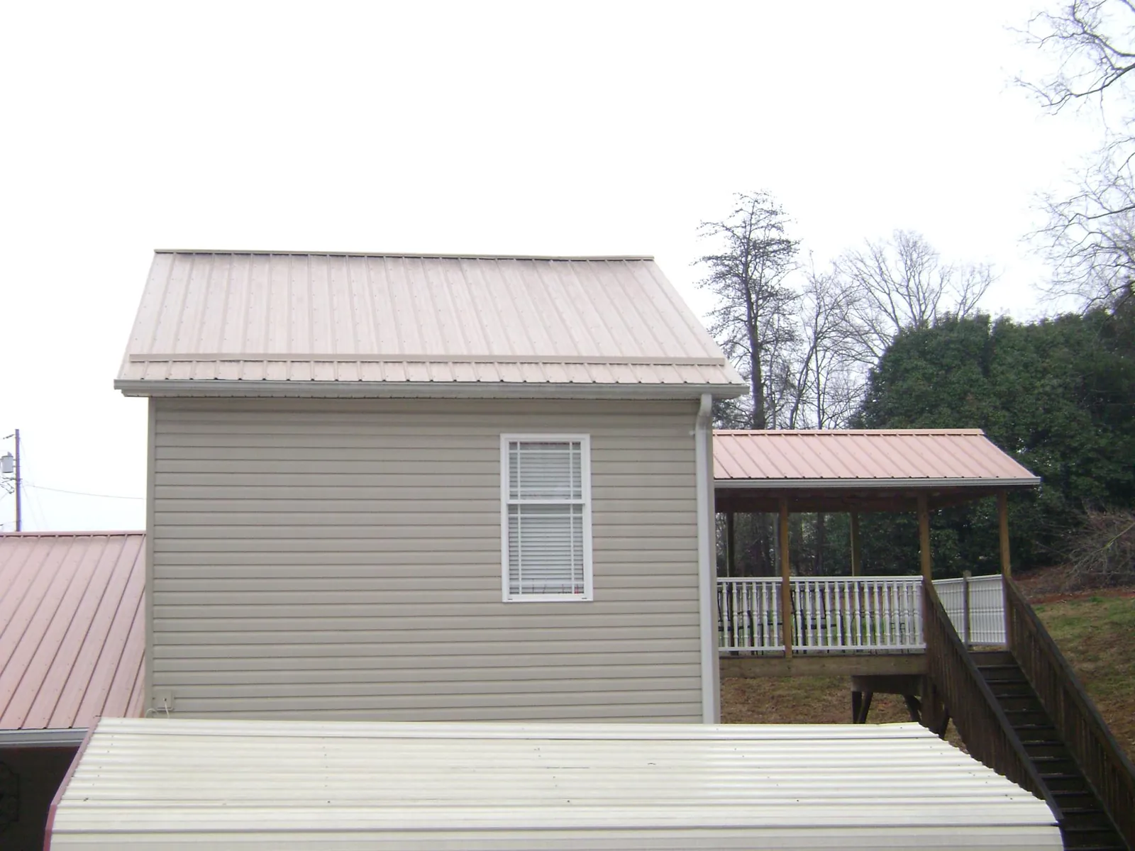 Tan metal roofs on a two story addition and attached porch, from a Roof Replacement job in Carrsville